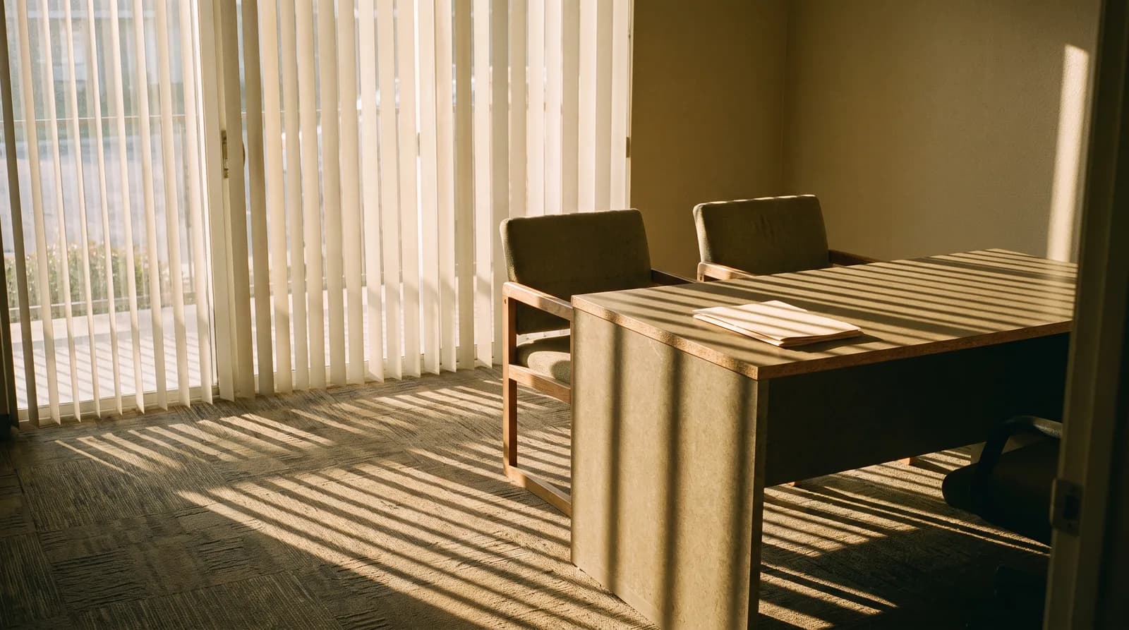 An empty leasing office with a plain desk, two chairs, and a closed folder.