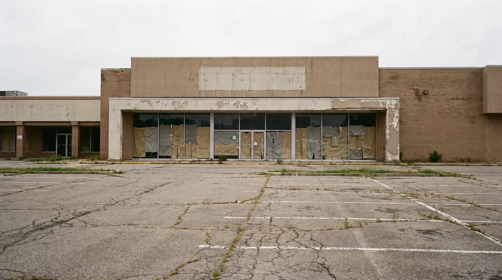 A vacant former anchor storefront with papered-over windows at the end of an older center.